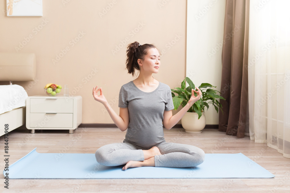 Beautiful young asian pregnant woman doing yoga exercise lotus pose on the blue yoga mat at home. Pregnancy, meditation, calmness concept Beautiful young asian pregnant woman doing yoga exercise lotus pose on the blue yoga mat at home. Pregnancy, meditation, calmness concept
