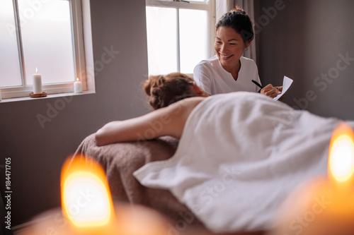 Female massage therapist talking to woman at wellness center