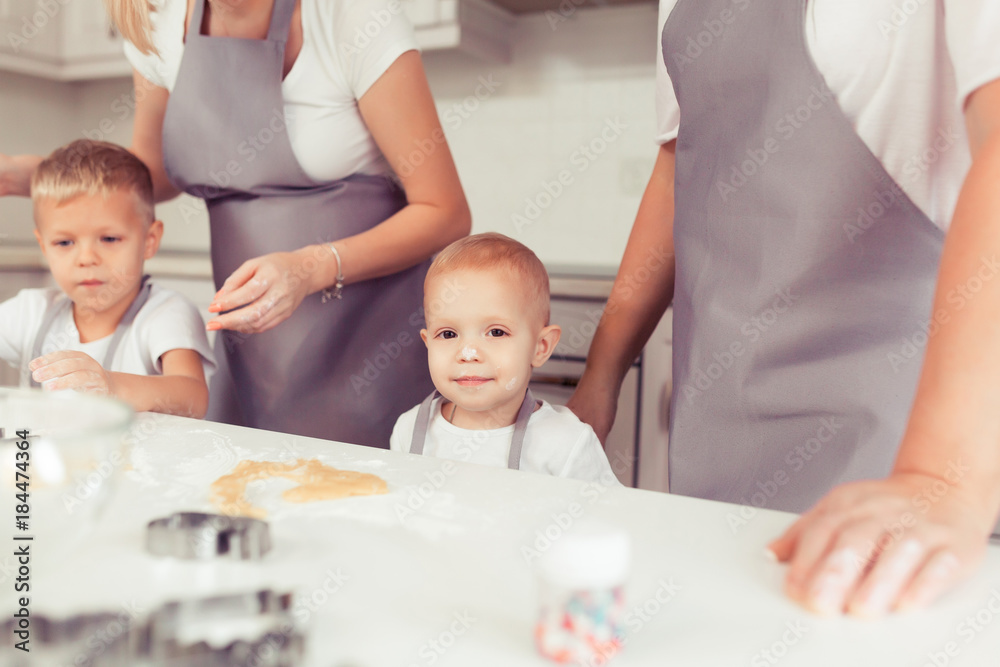 Cooking gingerbread cookies at home in the white kitchen. Happy family of mother, grandmother and little kids boys in the kitchen. Mom, grandma and children sons cooking together