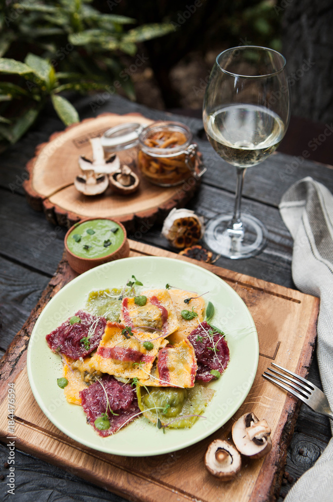 rustic composition: colorful ravioli with mushrooms on a wooden table with a glass of white wine