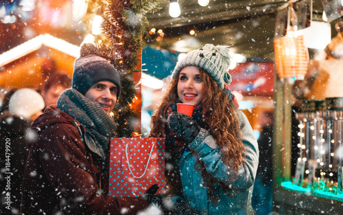 Christmas market restaurant at evening with snowfall, couple with hot drinks in fairy surroundings