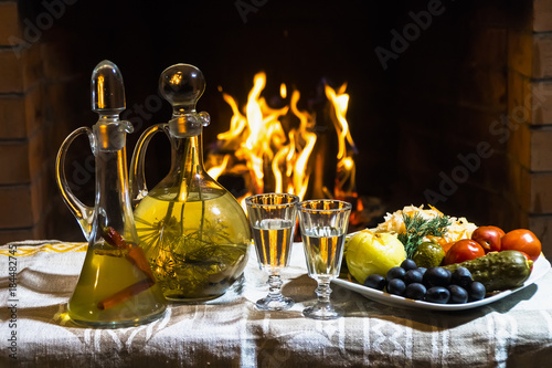 Fototapeta Naklejka Na Ścianę i Meble -  Traditional homemade Russion  herbal infused vodka with cold snacks and firplace on background