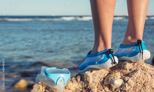 Female feet in aqua shoes near reefs and corals . Water sports equipment.
