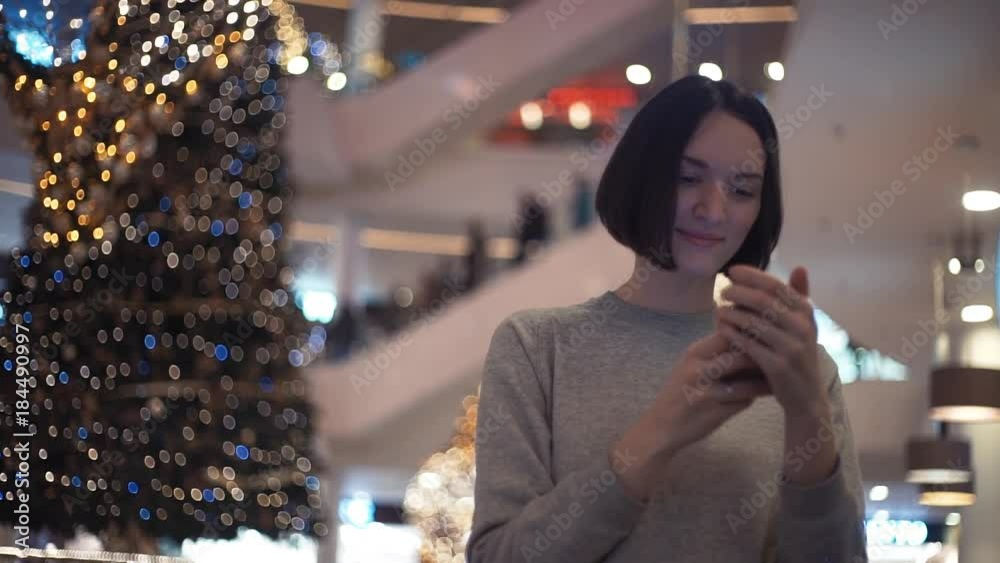 Attractive young woman smiling using smartphone in a crowded shopping mall. Attractive young woman smiling using smartphone in a crowded shopping mall.