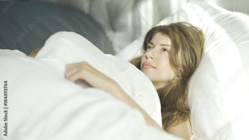Beautiful young woman is sleeping on a white pillow. She is waking up and smiling. Handheld real time medium shot Beautiful young woman is sleeping on a white pillow. She is waking up and smiling. Handheld real time medium shot
