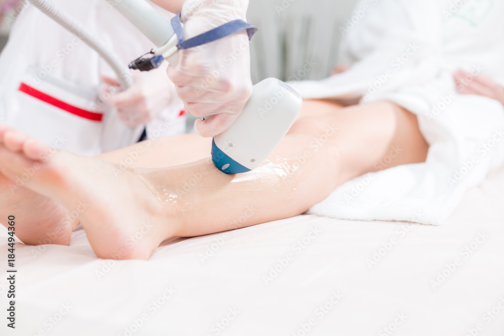 Naklejka premium Doctor cosmetologist makes the procedure a young girl blonde. Laser epilation and cosmetology. Hair removal on ladies legs. at cosmetic beauty spa clinic.