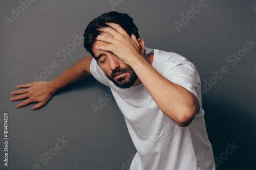 Man suffering from dizziness with difficulty standing up while leaning on wall photo