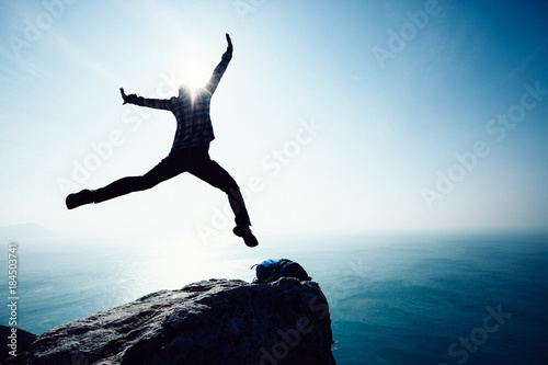 free female hiker jumping on sunrise seaside cliff edge
