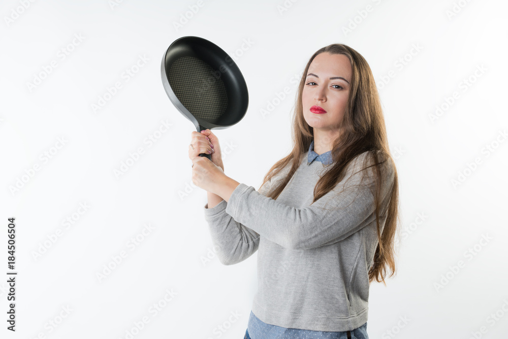 Angry young pretty woman with rage, umbragem, insult on her face and frying pan in her hand. She is punching to the camera. Angry young pretty woman with rage, umbragem, insult on her face and frying pan in her hand. She is punching to the camera.