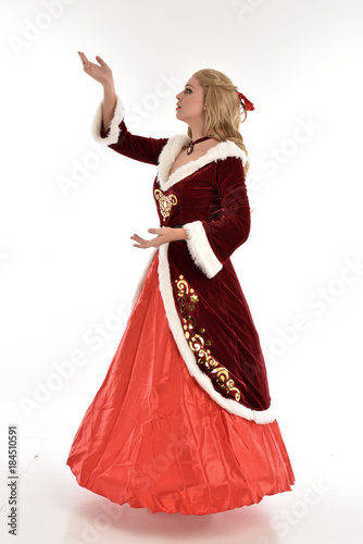  full length portrait of pretty blonde lady wearing red and white christmas inspired costume gown, standing pose on white background.