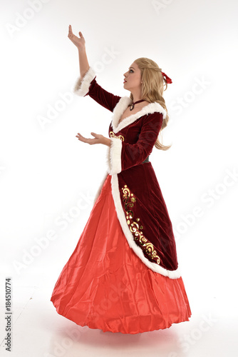  full length portrait of pretty blonde lady wearing red and white christmas inspired costume gown, standing pose on white background.
