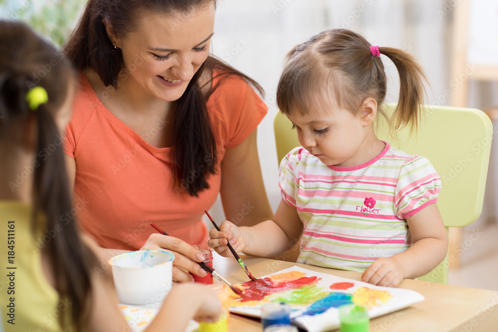 Teacher and little girls are painting in daycare center. Woman and children have a fun pastime. Teacher and little girls are painting in daycare center. Woman and children have a fun pastime.