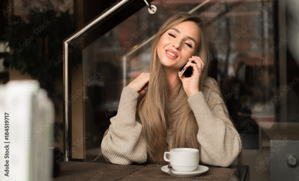 Young happy woman talking on mobile phone with friend while sitting alone in modern coffee shop interior, smiling hipster girl calling with cell telephone while relaxing after walking in summer day Young happy woman talking on mobile phone with friend while sitting alone in modern coffee shop interior, smiling hipster girl calling with cell telephone while relaxing after walking in summer day