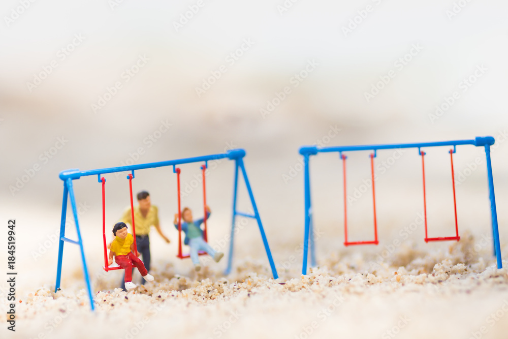 Miniature people : Children are playing swings happily. Father takes care of the back on the sand beach. Miniature people : Children are playing swings happily. Father takes care of the back on the sand beach.