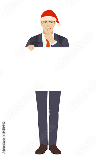 Businessman in Santa hat holding white blank poster and making hush sign