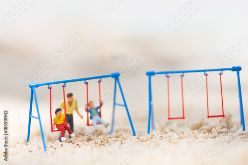 Miniature people : Children are playing swings happily. Father takes care of the back on the sand beach.