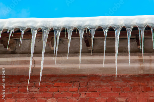 White snow on the roof of a red brick house and icicles hanging from a slate roof