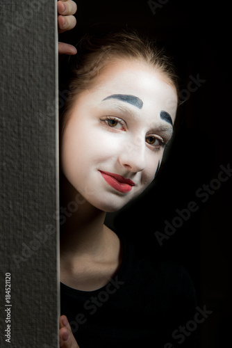 The girl wth makeup of mime hiding behind the wall