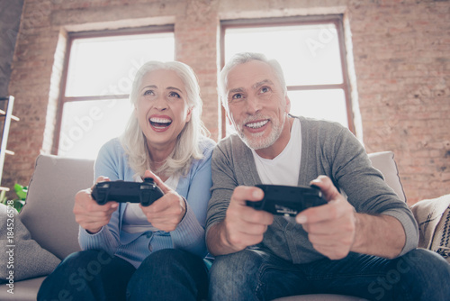 Excited concentrated middle-aged couple sitting on a couch in their living room in front of the television screen playing video games with joy stick photo