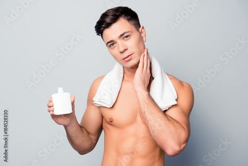 Fresh and handsome. Portrait of confident sexy stunning sporty young guy with a white towel on shoulders, he is applying a lotion after shaving on his soft smooth skin, isolated on grey background photo