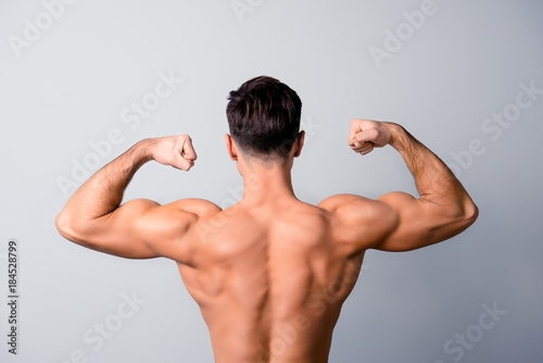 I am in favour of healthy lifestyle, sport, diet and nutrition! Back view photo of handsome confident man showing his muscular arms, isolated on grey background