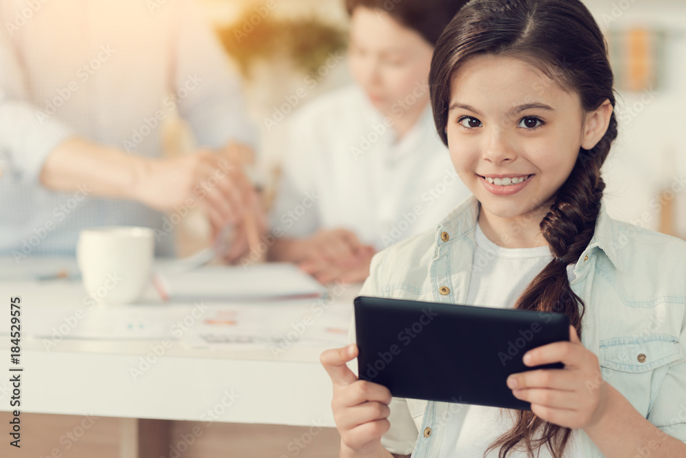 Friendly girl. Cheerful pretty nice girl holding a tablet and smiling to you while being in a positive mood Friendly girl. Cheerful pretty nice girl holding a tablet and smiling to you while being in a positive mood