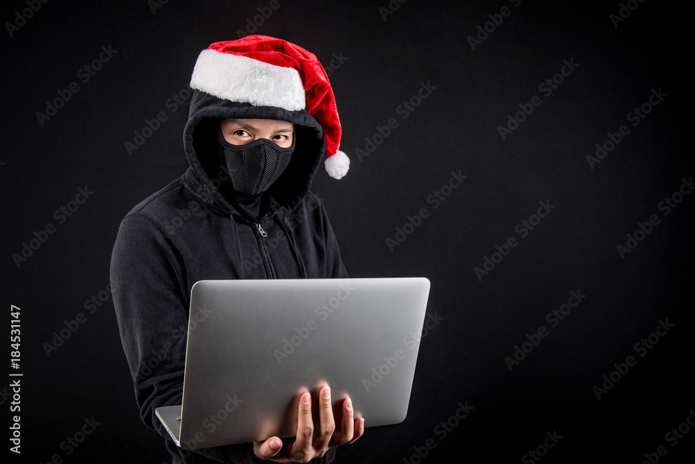 Mysterious male santa hacker holding laptop computer, anonymous man on black background, ransomware cyber attack and internet security on Christmas holiday concepts Mysterious male santa hacker holding laptop computer, anonymous man on black background, ransomware cyber attack and internet security on Christmas holiday concepts