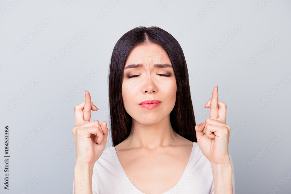 Close up portrait of pretty young woman closed her eyes and making wish, having her fingers crossed, worry about result, outcome, standing over grey background Close up portrait of pretty young woman closed her eyes and making wish, having her fingers crossed, worry about result, outcome, standing over grey background