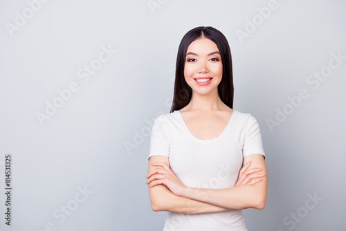 Portrait of cute confident pretty woman with beaming smile with folded hands, standing over grey background with copy space