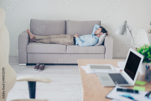 Concept of necessity of  having a rest while working. Tired exhausted manager clothed in formal-wear is sleeping on a sofa in his modern office photo