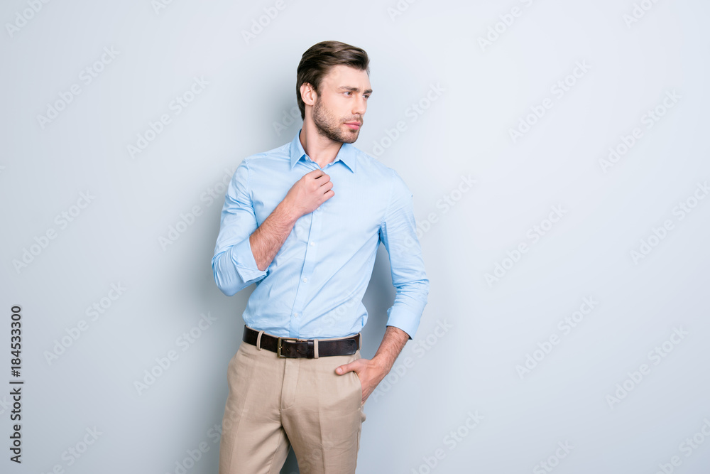 Fototapeta premium Stunning, perfect man holding one face on button and another one in pocket, looking to the side over grey background