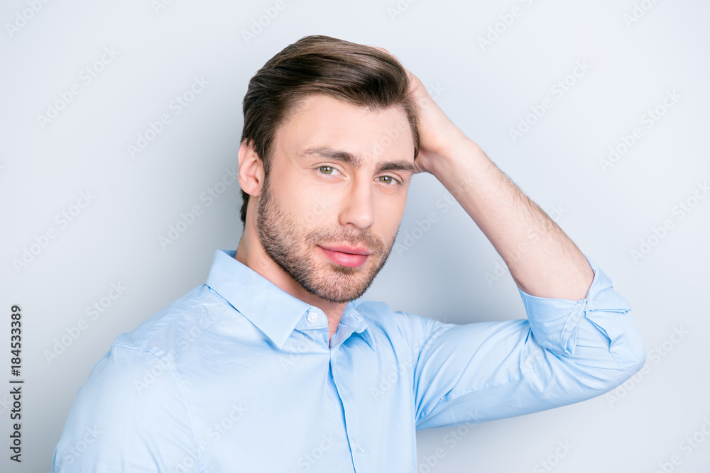 Close up portrait of attractive man touching his perfect hair and looking to the camera while standing over grey background Close up portrait of attractive man touching his perfect hair and looking to the camera while standing over grey background
