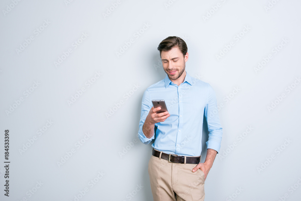Portrait with copy space of attractive, cute man holding smart phone in one hand and another one in pocket, checking email through wifi, 3G internet over grey background Portrait with copy space of attractive, cute man holding smart phone in one hand and another one in pocket, checking email through wifi, 3G internet over grey background