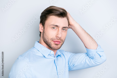 Close up portrait of attractive man touching his perfect hair and looking to the camera while standing over grey background