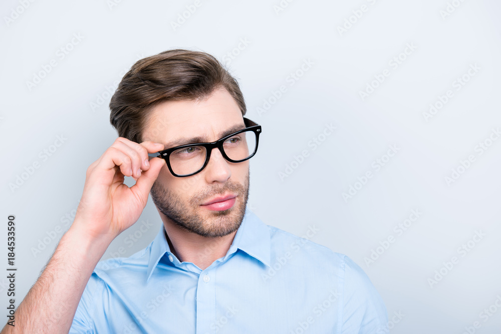 Close up portrait with copy space of attractive, clever, perfect man in shirt and glasses holding eyelet of spectacles on his face looking to the side over grey background Close up portrait with copy space of attractive, clever, perfect man in shirt and glasses holding eyelet of spectacles on his face looking to the side over grey background