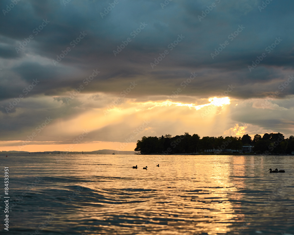 Sun breaking through low hanging storm clouds during sunset over Lake Constance