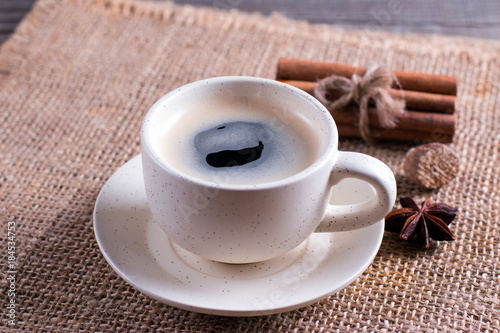 Cup of coffee with cinnamon tubes on wooden table