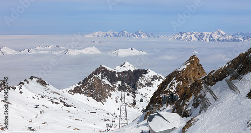 Austria, Zell Am See, Kaprun - March 21, 2017: High-altitude Gletscher-Shuttle and GletscherJet 4 lifts above ski slopes with foggy Alps Mountains and blue sky in background at Kitzsteinhorn glacier