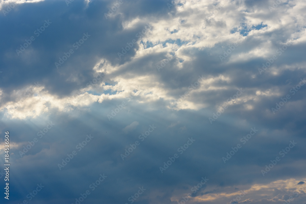 The sun's rays against the blue sky make their way through clouds and clouds