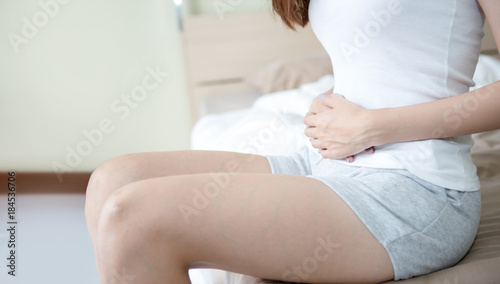 Young woman having a period cramps or period pain or stomachache lie down on her bed