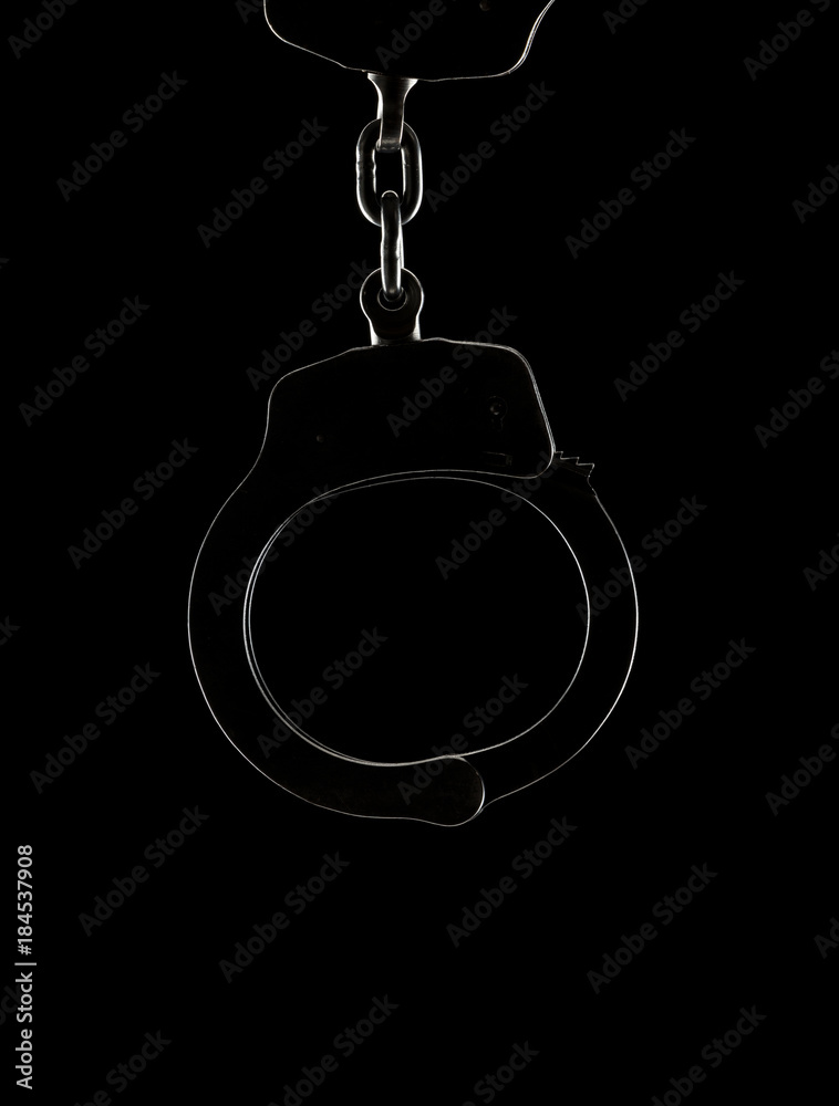Backlit handcuff silhouette on a black background with copy space below handcuffs Backlit handcuff silhouette on a black background with copy space below handcuffs