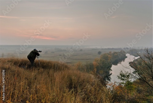 the photographer is shooting the autumn landscape with the sunrise by the river © Oleg Pavlov