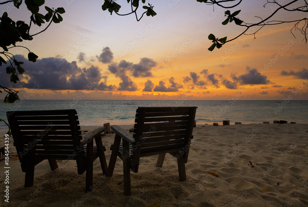 Two wooden chairs on a tropical beach during sunset, low key light