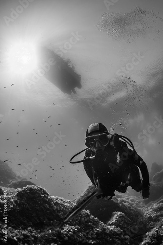 woman scuba diving over rocks in the Mediterranean Sea with a boat on the surface dans sun rays photo