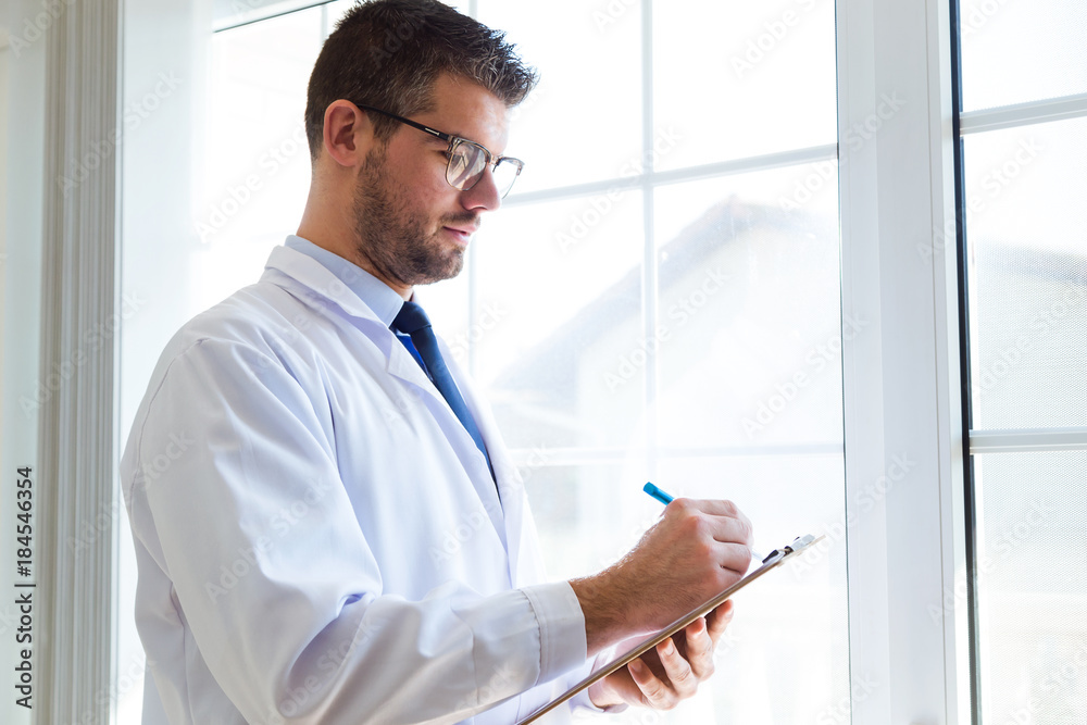 Confident male doctor writing information of his patient in the office.