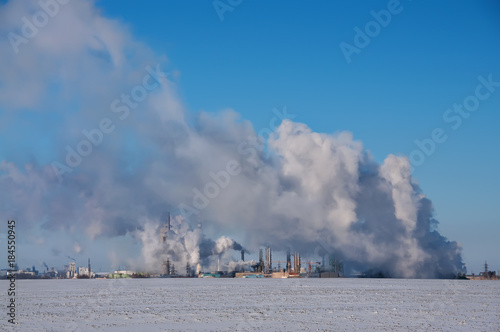 Steam wallows with the production, heat complex in the winter. A production complex standing in the middle of a snow-covered field. Industrial buildings and smoking pipes 