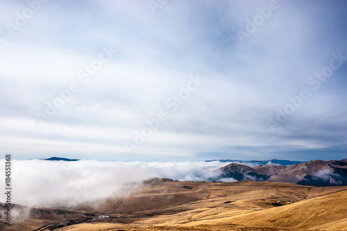 A tranquil mountain scene with clouds cover on a hill. Some cabins in the backgroud