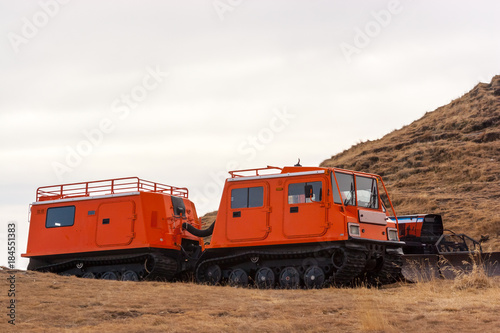 Orange snowcat with second wagon. Another vehicle with snowplow seen in the background