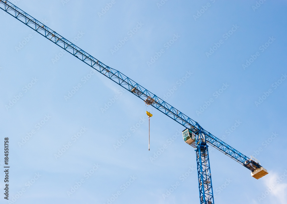 Industrial construction crane hoisting against blue sky Industrial construction crane hoisting against blue sky