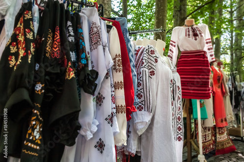 Multiple profile of romanian traditional costumes on mannequins and hangers shown outdoors